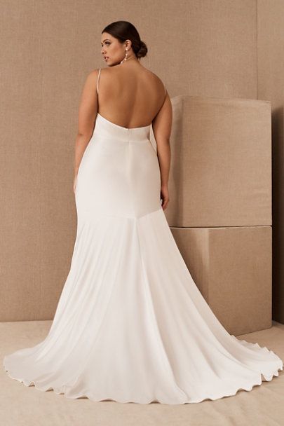 a woman in a white wedding dress leaning against a wall with her back to the camera