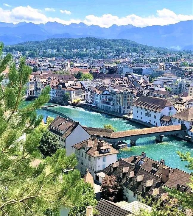 a river running through a city next to tall buildings with mountains in the back ground