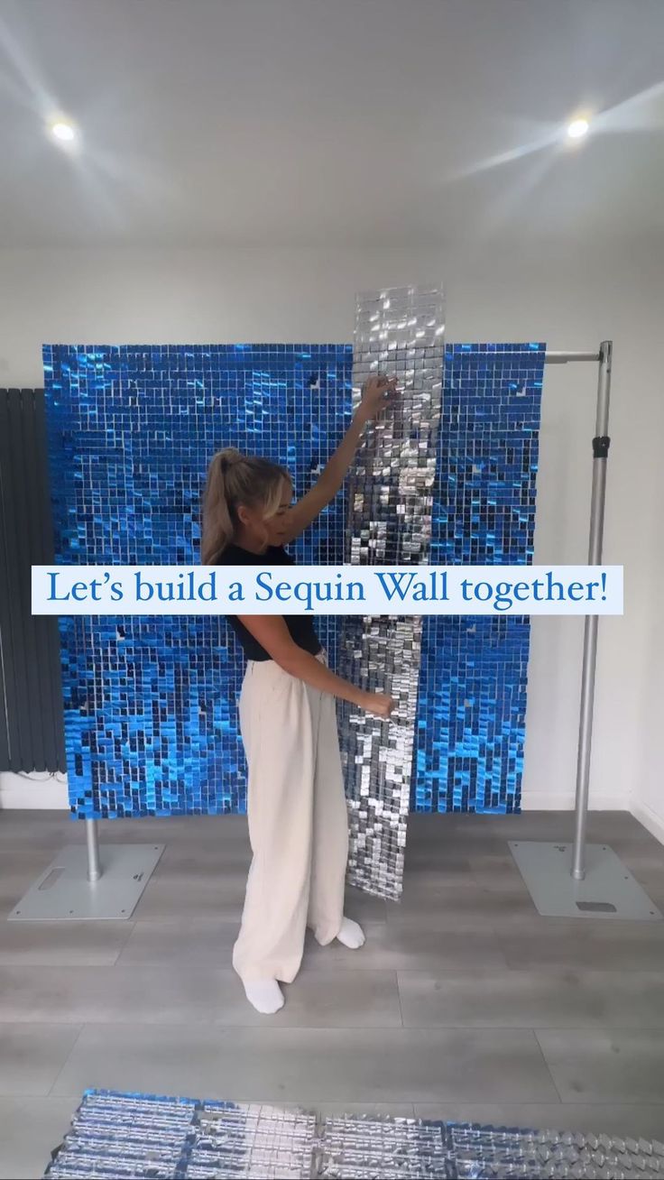 a woman standing in front of a blue mosaic tile wall with the words let's build a sequin wall together