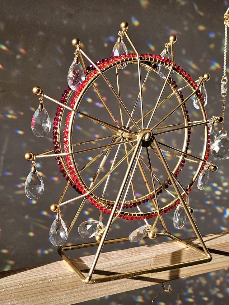 a miniature ferris wheel is sitting on top of a piece of wood with beads and chains hanging from it