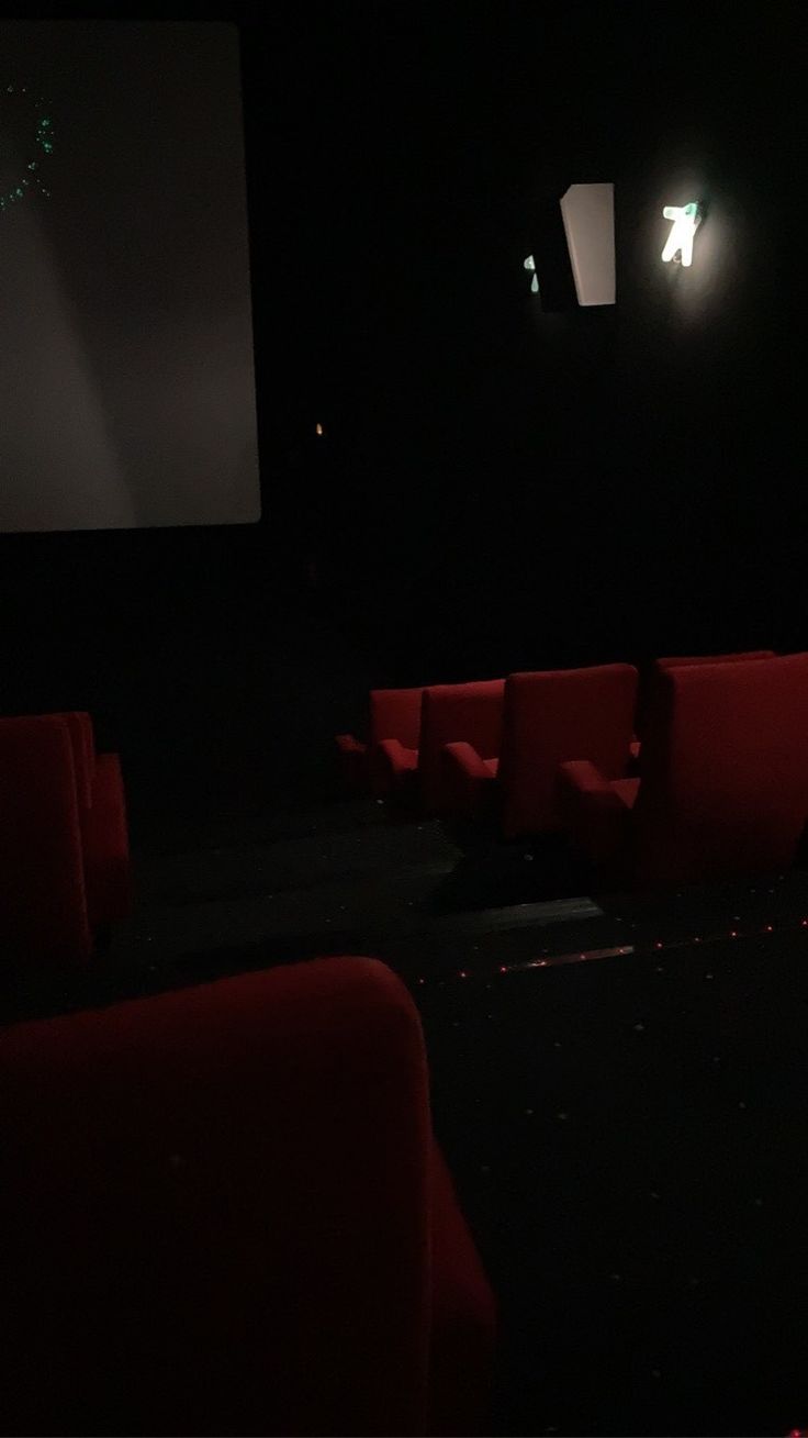 an empty movie theater with red seats and projector screen in the dark, at night