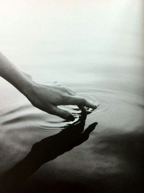 a black and white photo of a person's hand in the water with their reflection