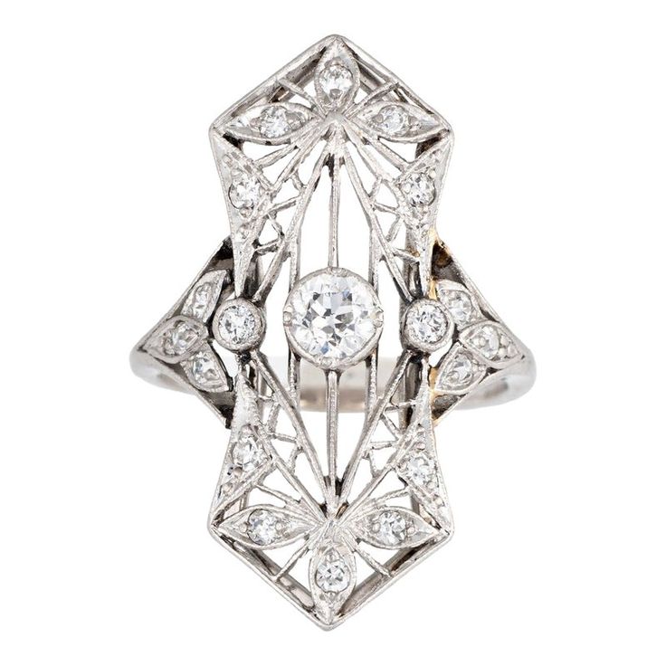 Finely detailed antique Edwardian ring (circa 1900s to 1910s) crafted in 900 platinum.   Centrally mounted estimated 0.25 carat old Mine cut diamond is accented with 18 x estimated 0.02 to 0.03 carat diamonds. The total diamond weight is estimated at 0.63 carats. The diamonds are estimated at H-I colour and SI1-2 clarity.   The ring features lacy filigree detail within an elongated shield mount, a hallmark of the Edwardian era. With a slight curved saddle the ring sits comfortably on the finger Andromeda Black, Edwardian Diamond Ring, Diamond Ring Platinum, Edwardian Ring, Antique Jewelry Rings, Old Mine Cut Diamond, Vintage Fine Jewelry, Ring Flower, Antique Ring