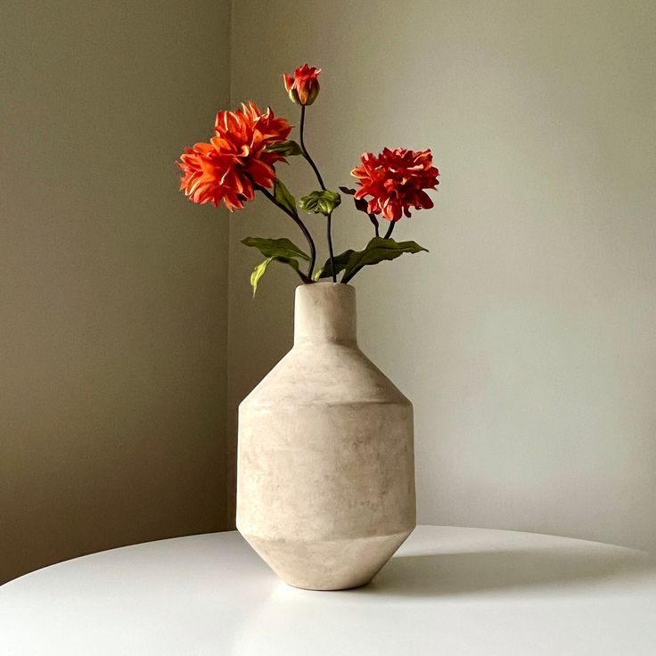 a white vase with some red flowers in it