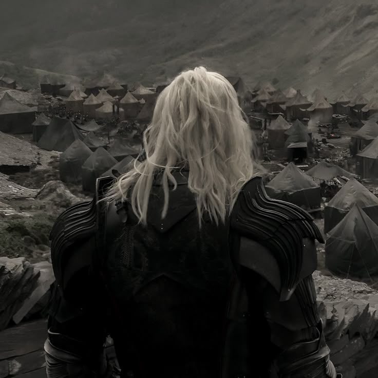 a woman with long blonde hair standing in front of a camp site and looking at the mountains