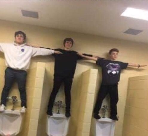 three young men standing on urinals in a bathroom with their arms around each other