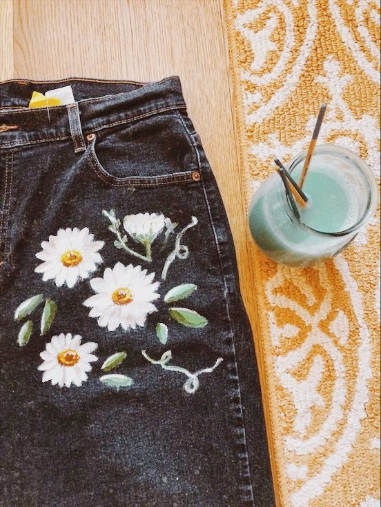 a pair of jeans with flowers painted on them next to a cup and strawberries