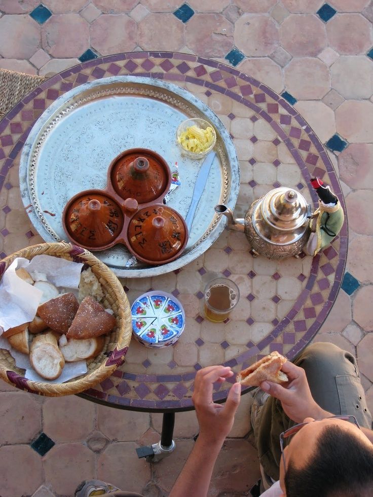 a person sitting at a table with some food on it and teapots next to them