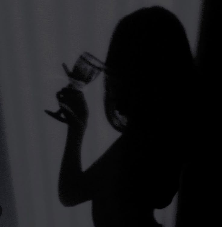 the silhouette of a woman holding a wine glass in her right hand and looking down