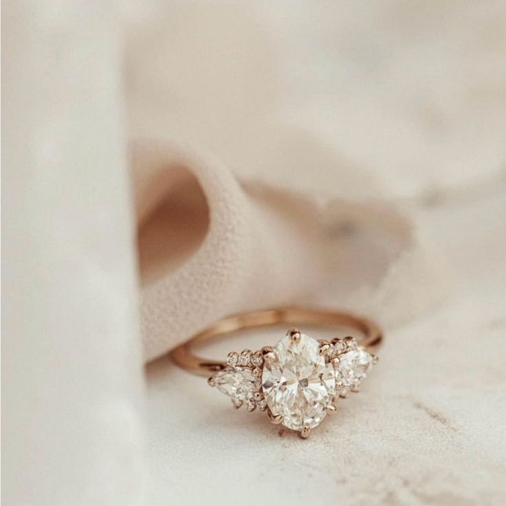 an engagement ring with three pear shaped diamonds on it, sitting next to a white cloth