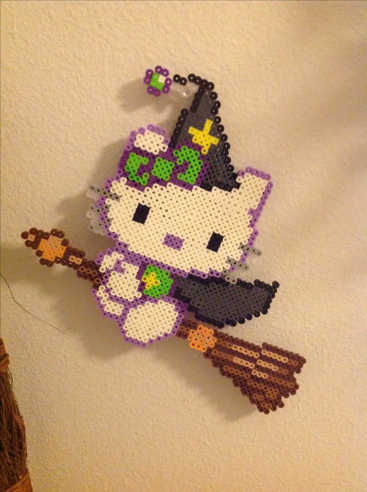 a cross stitch hello kitty with a witch hat and broom hanging on the wall next to a potted plant