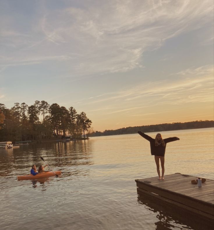 a woman standing on top of a wooden dock next to a body of water with two kayaks