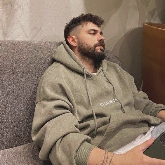 a man with a beard sitting on a couch holding a laptop computer and looking off to the side