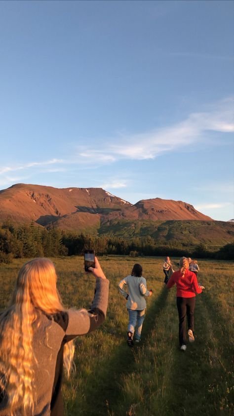 three people are walking in the grass with their cell phones up to their ears and one person is taking a photo