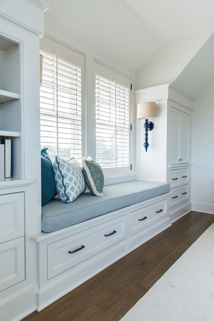 a window seat in the corner of a room with white drawers and blue pillows on it