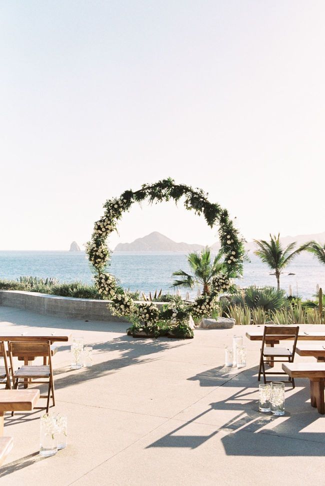 an outdoor ceremony setup with wooden benches and greenery on the ground, overlooking the ocean