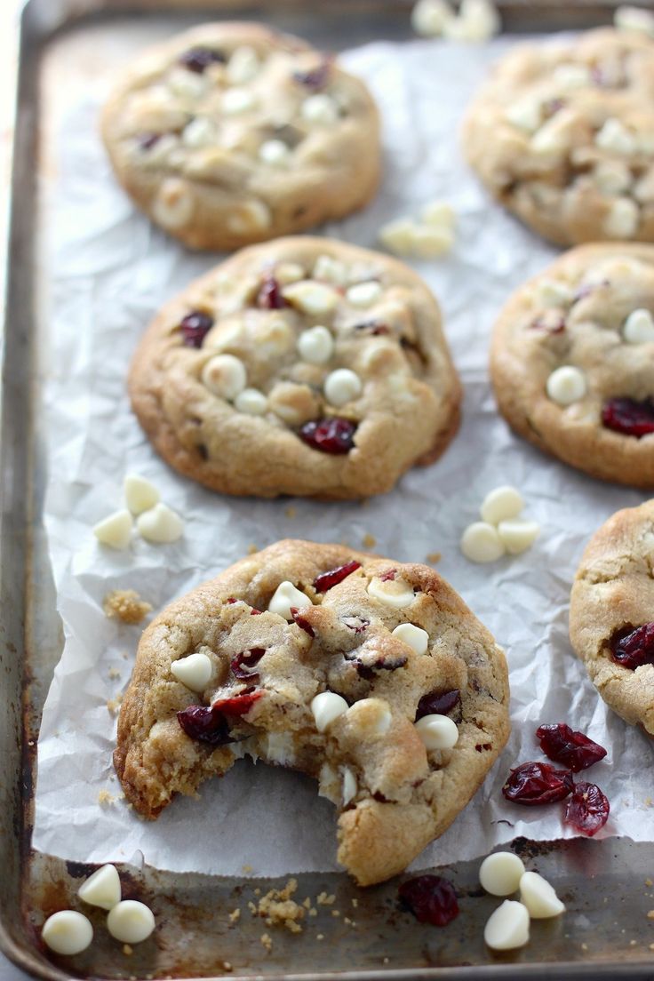 cookies with white chocolate chips and cranberries are on a baking sheet, ready to be eaten