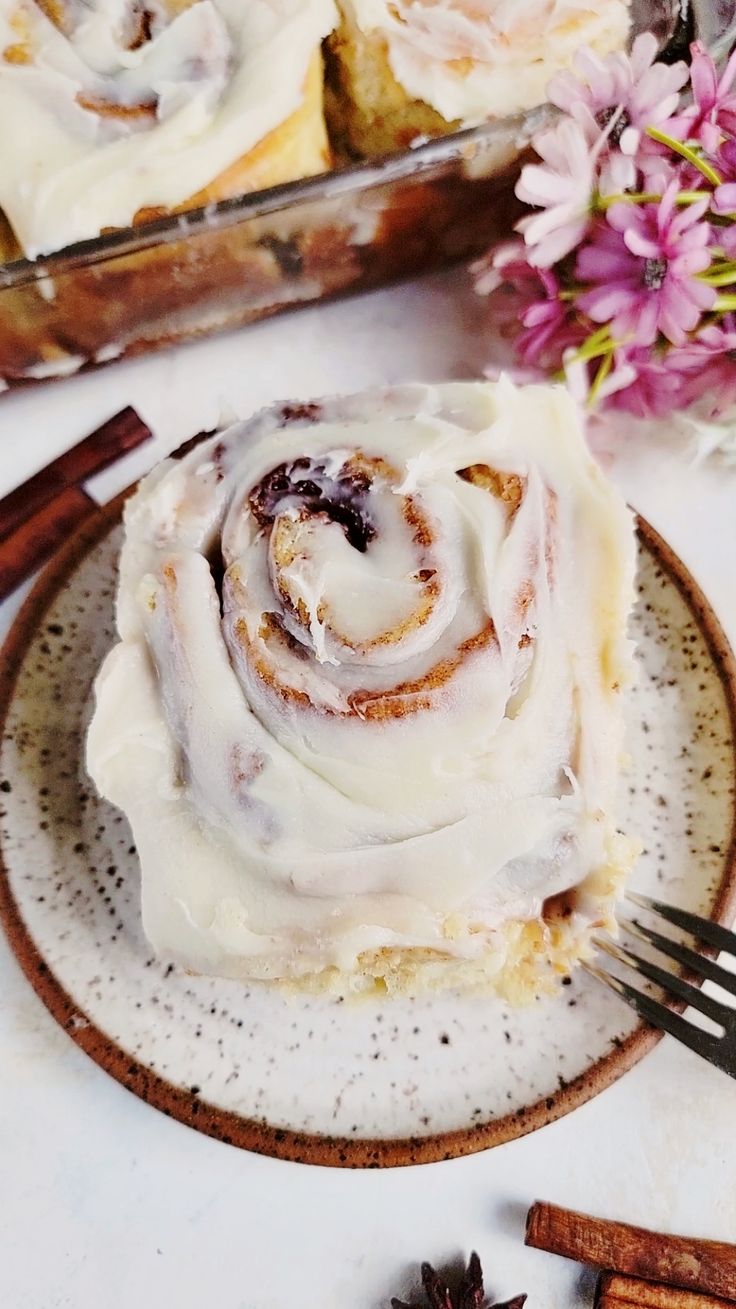 a cinnamon roll sitting on top of a white plate next to some cinnamon sticks and flowers