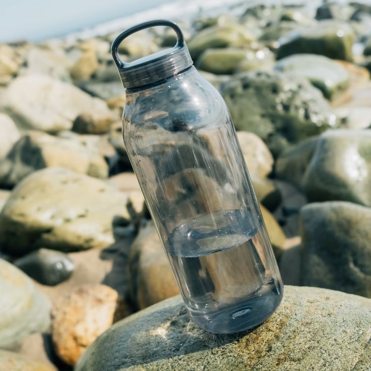 a water bottle sitting on top of a rock next to the ocean with rocks in it