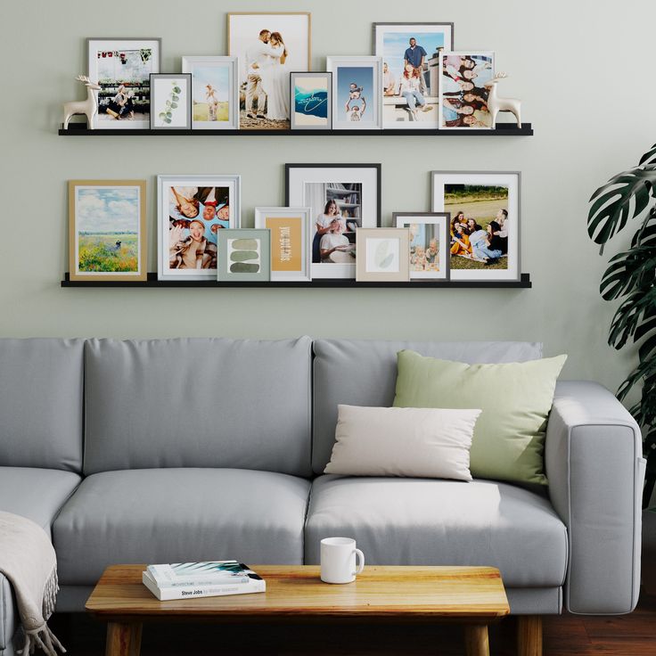 a gray couch sitting in front of a wooden table with pictures on the wall above it