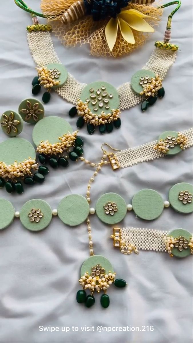 some green and gold necklaces are laying on a white sheet with flowers in the background