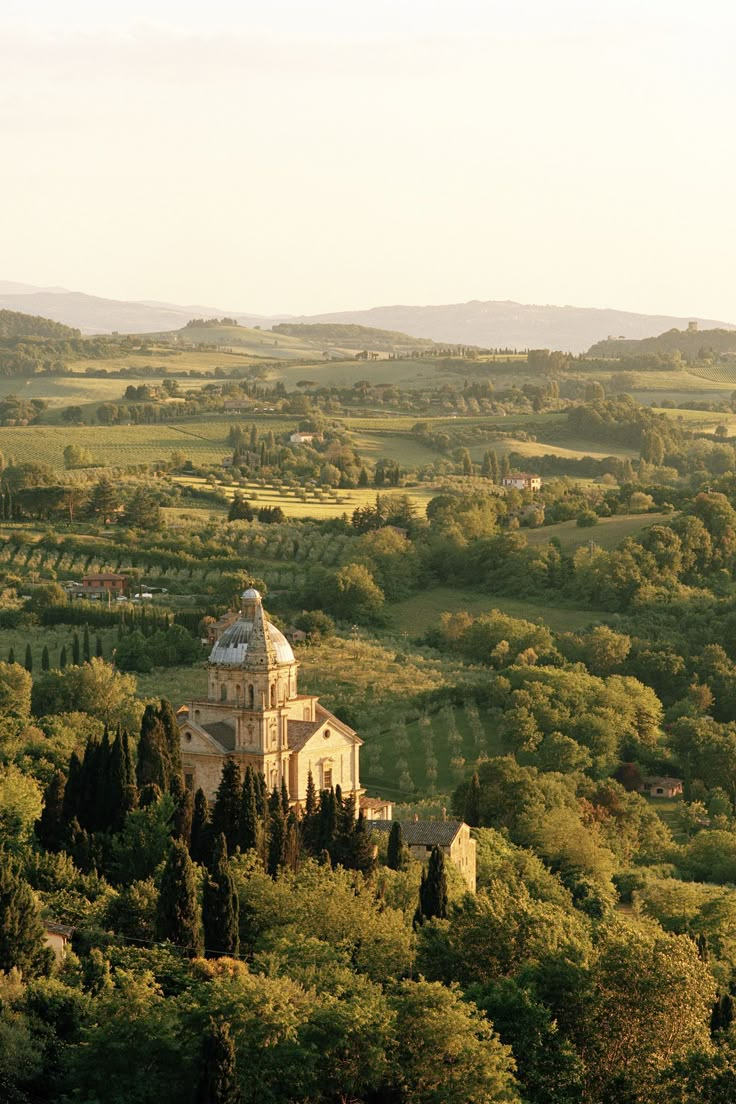 an old church surrounded by trees in the middle of a green valley with rolling hills