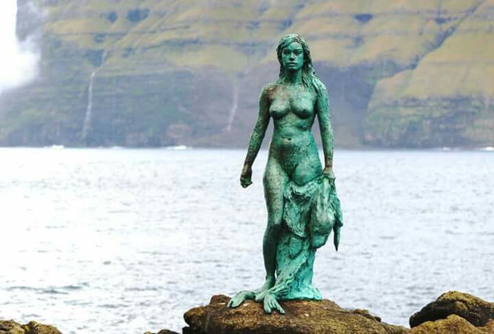 a statue is standing on some rocks by the water