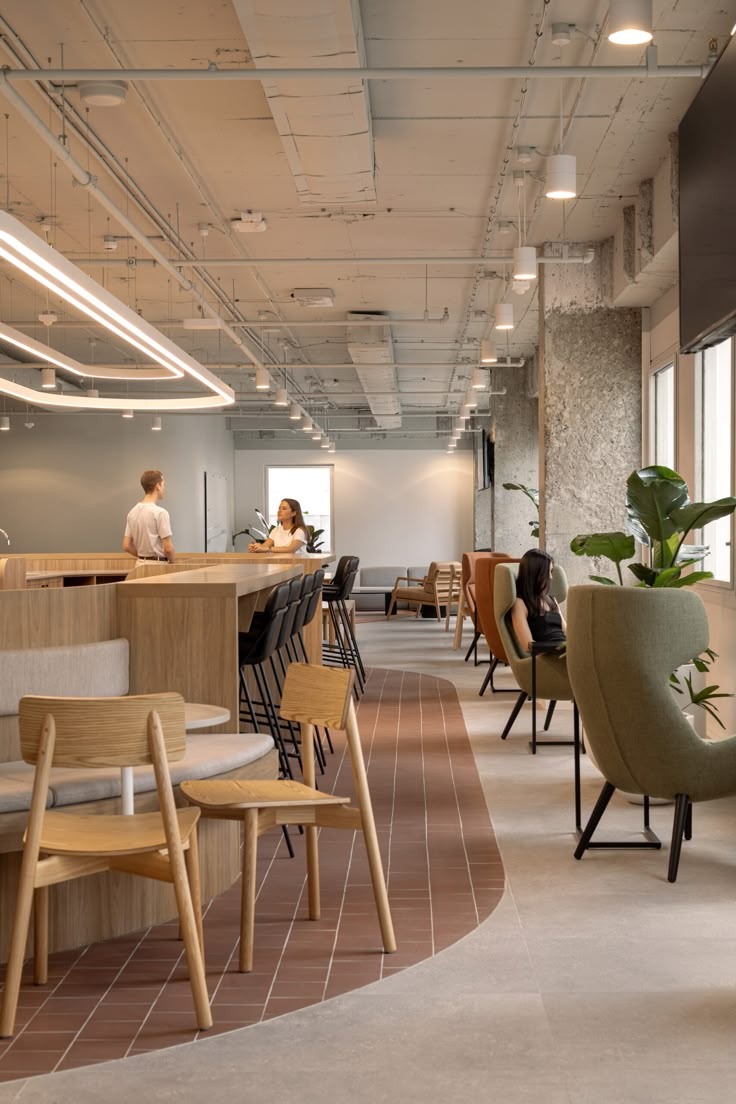 an office with chairs, desks and people sitting at the counter in front of large windows