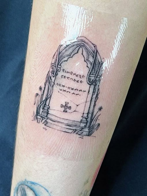 a person with a tattoo on their arm that has a grave in the ground and words written below it