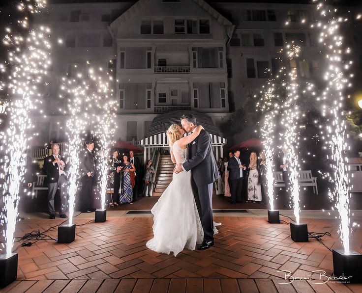 a bride and groom kissing in front of their wedding party with sparklers on the ground