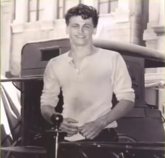 black and white photograph of a man standing in front of an old car with his hand on the handle