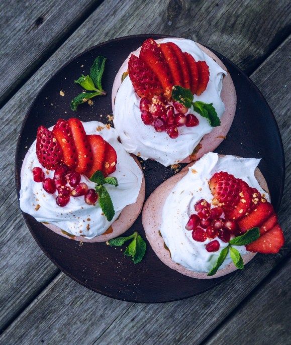 three desserts with strawberries and whipped cream on a black plate sitting on a wooden table