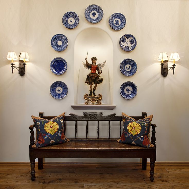 a wooden bench sitting in front of a wall with plates on it and an angel statue