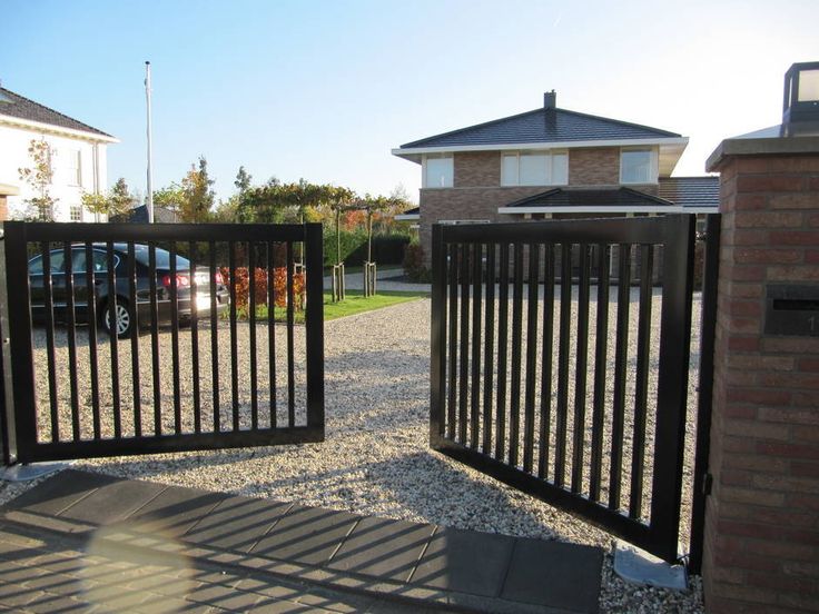 an iron gate in front of a brick house with cars parked on the driveway behind it