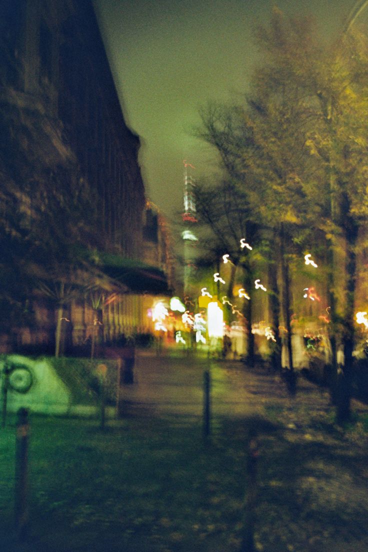 a blurry photo of a park at night with trees and buildings in the background