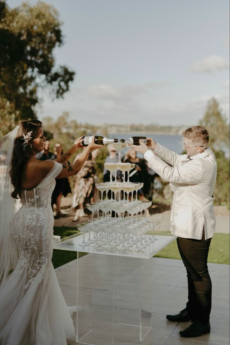 the bride and groom are taking pictures with their wine glasses as they stand in front of an outdoor wedding cake