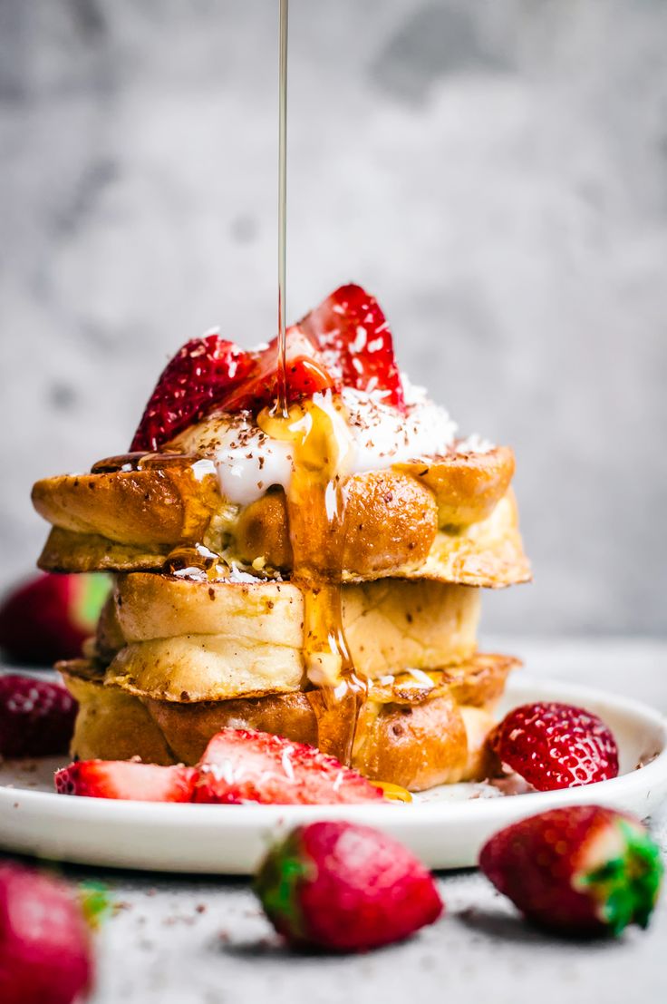 a stack of french toast with strawberries and syrup being drizzled on top