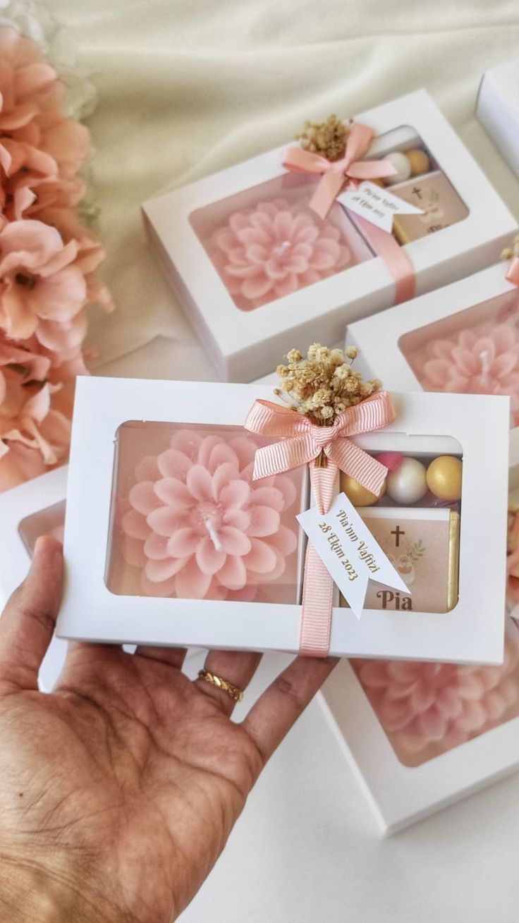 three boxes with pink flowers in them on a white tablecloth and two hands holding the box