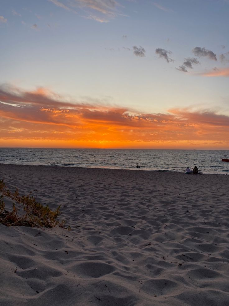 the sun is setting at the beach with people in the water and on the sand