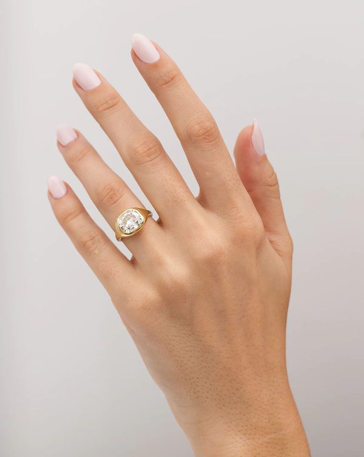 a woman's hand wearing a gold ring with a white diamond on the middle