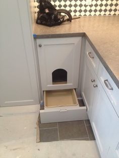 a dog house built into the side of a kitchen counter with its door open to reveal it's litter