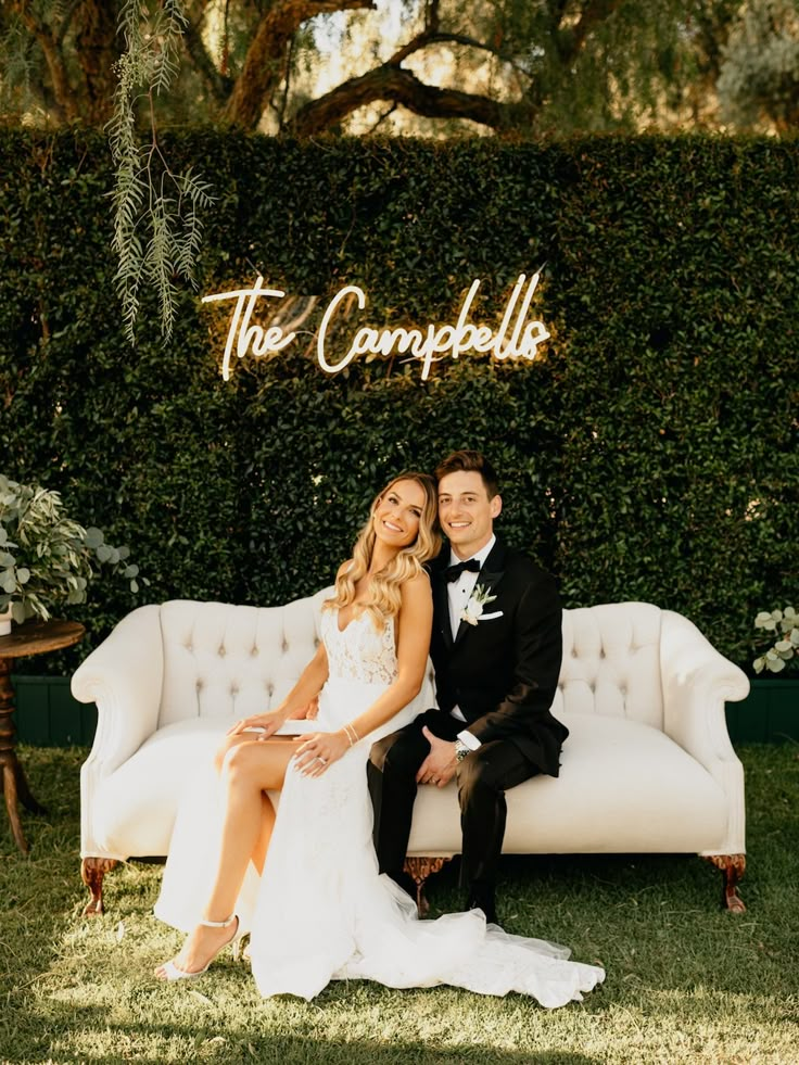 a bride and groom sitting on a couch in front of a sign that says the campbells