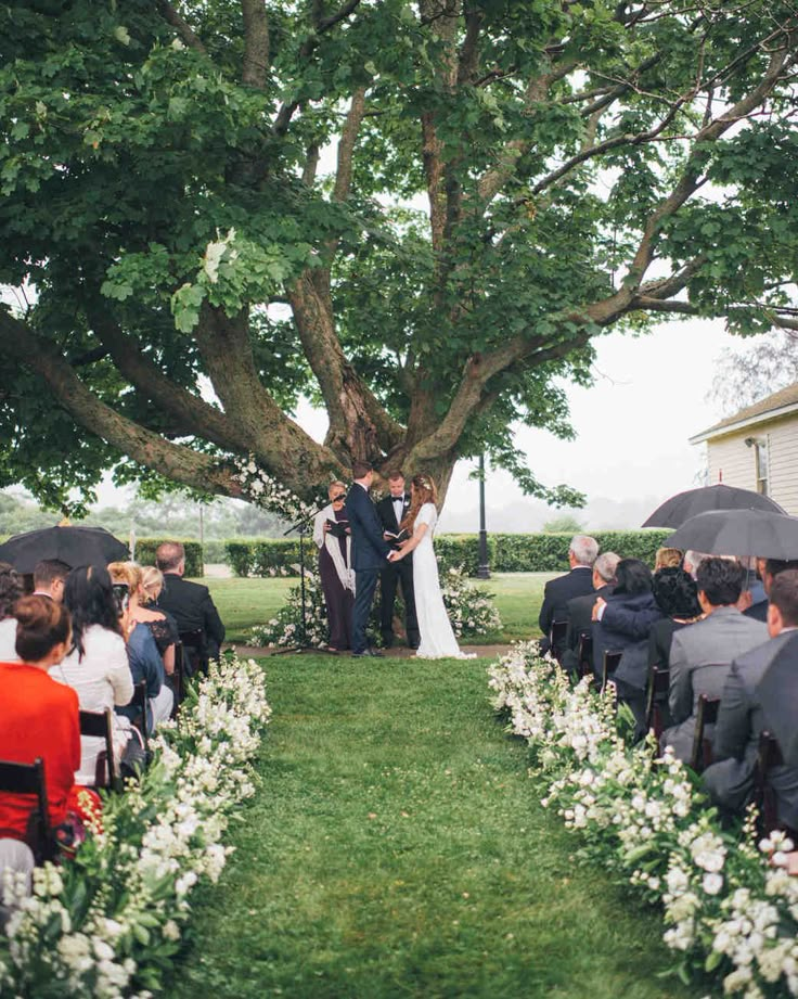 a bride and groom standing under a large tree at their wedding ceremony in the rain