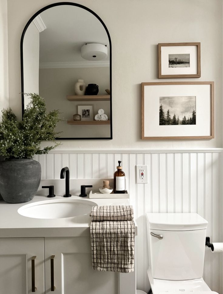 a bathroom with a toilet, sink, mirror and pictures on the wall above it