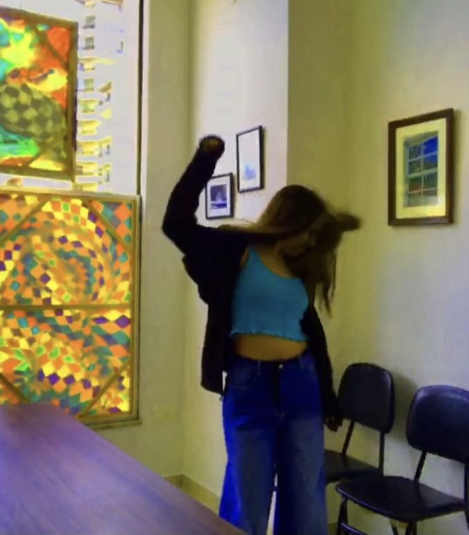 a woman standing next to a wooden table in front of a wall with pictures on it