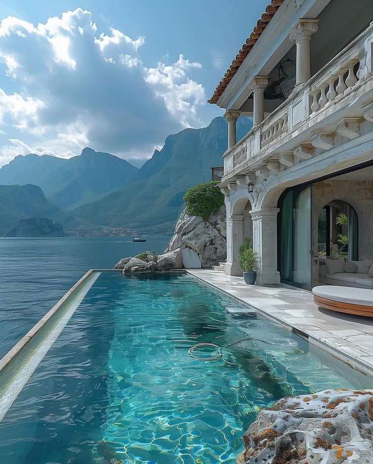 an outdoor swimming pool in front of a large house with mountains in the back ground