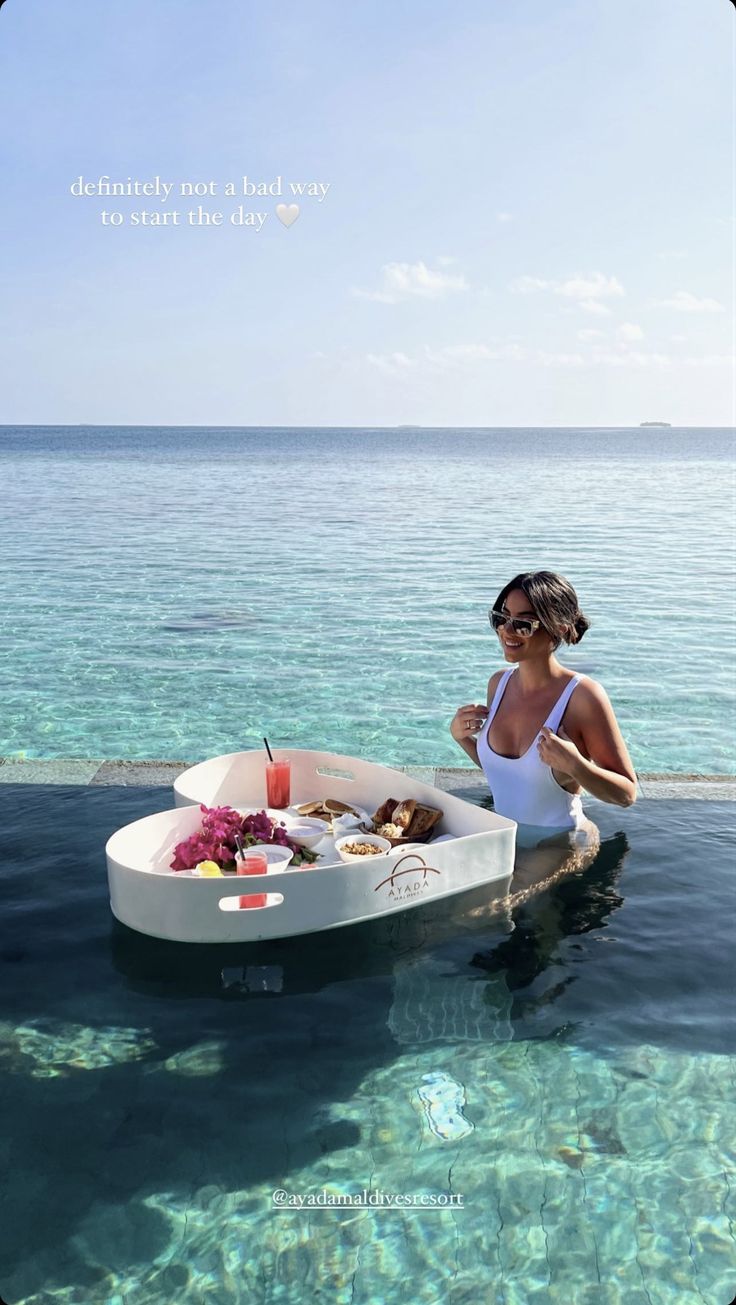 a woman sitting in the water with a boat full of food and drinks on it