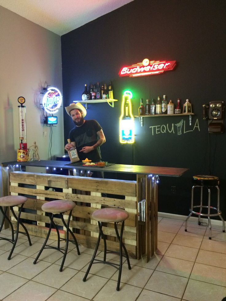 a man standing behind a bar with stools in front of it and neon signs on the wall