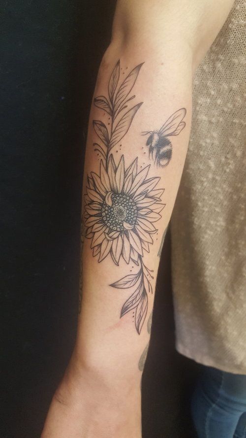 a person with a tattoo on their arm holding a bee and sunflower in front of them