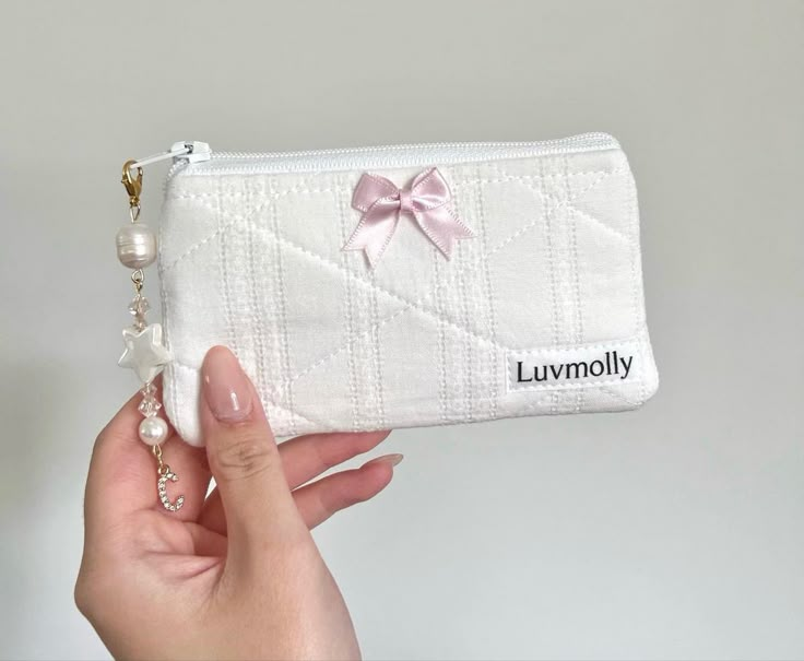 a hand holding a white purse with a pink bow on it